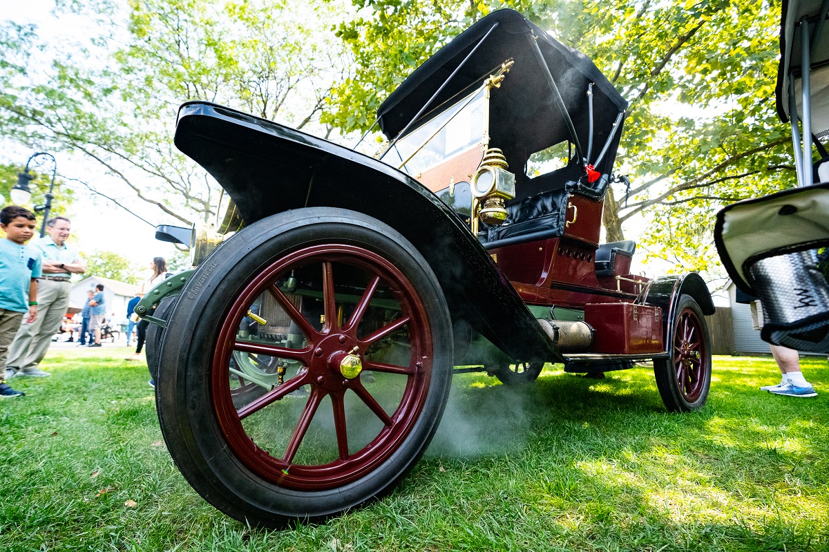 1909 White Model O at Old Car Festival 2021 Low-angle photograph of an old-fashioned largely open maroon car exudes steam as spectators look on