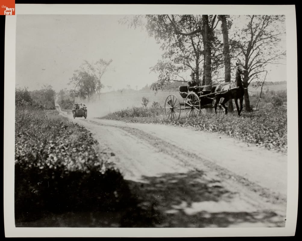 Automobile Passing Horse-Drawn Vehicle, circa 1912 Car in distance on dirt road between fields; a horse-drawn carriage is pulled over on one side