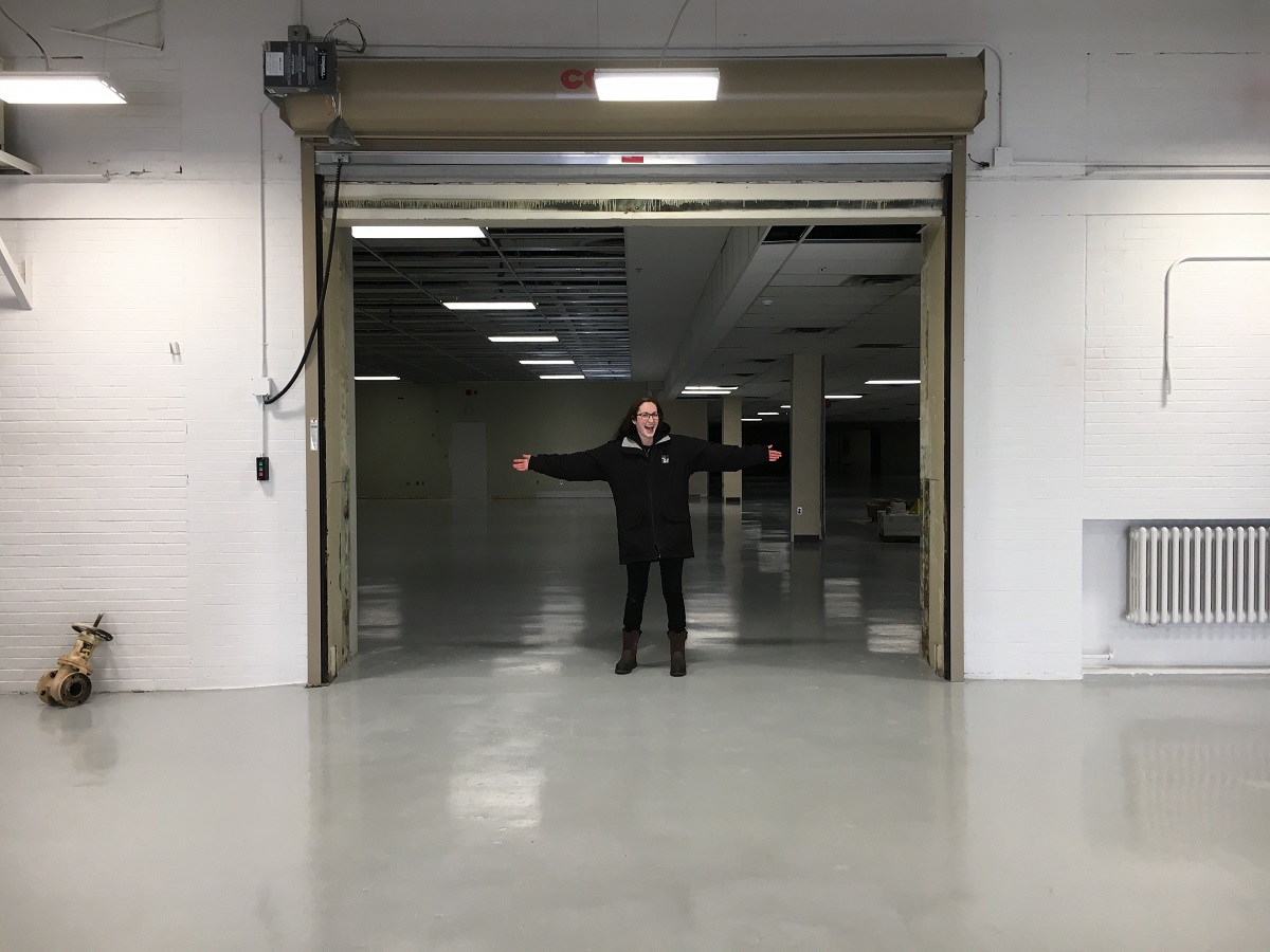 Our first day of possession for the Main Storage Building A person stands with arms outstretched in a large doorway connecting one large, empty room to another
