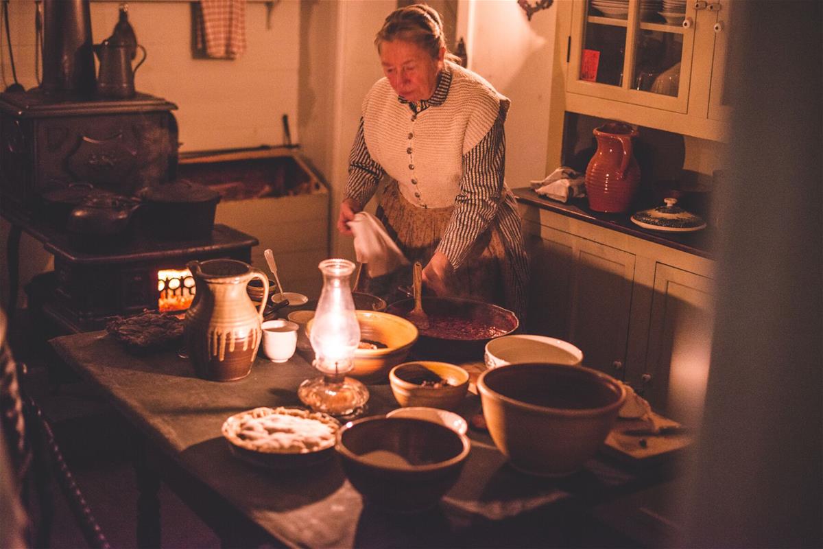 Woman in candlelit kitchen with a variety of bowls and plates containing food on kitchen table