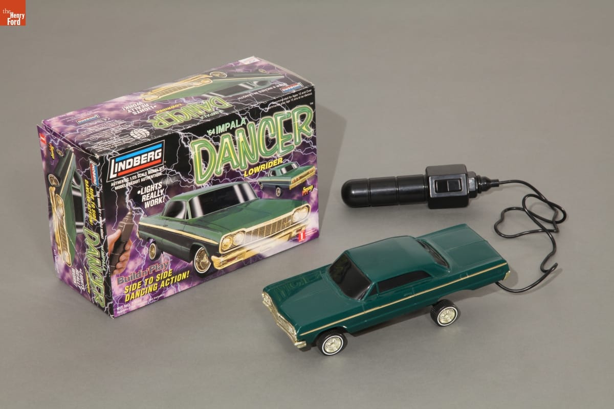 Dancin' 1964 Chevy Impala Model, circa 1999 Green car model connected by a wire to a black joystick-like object, in front of a purple, green, and black product box for the car