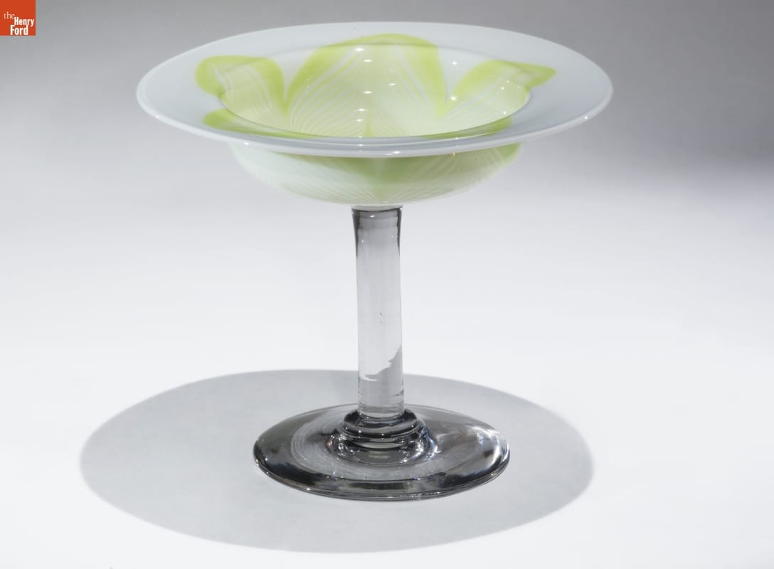 Compote, 1931-1935 Glass dish with thick transparent glass base and stem, topped with wide, shallow white glass bowl with swirling yellow-green pattern
