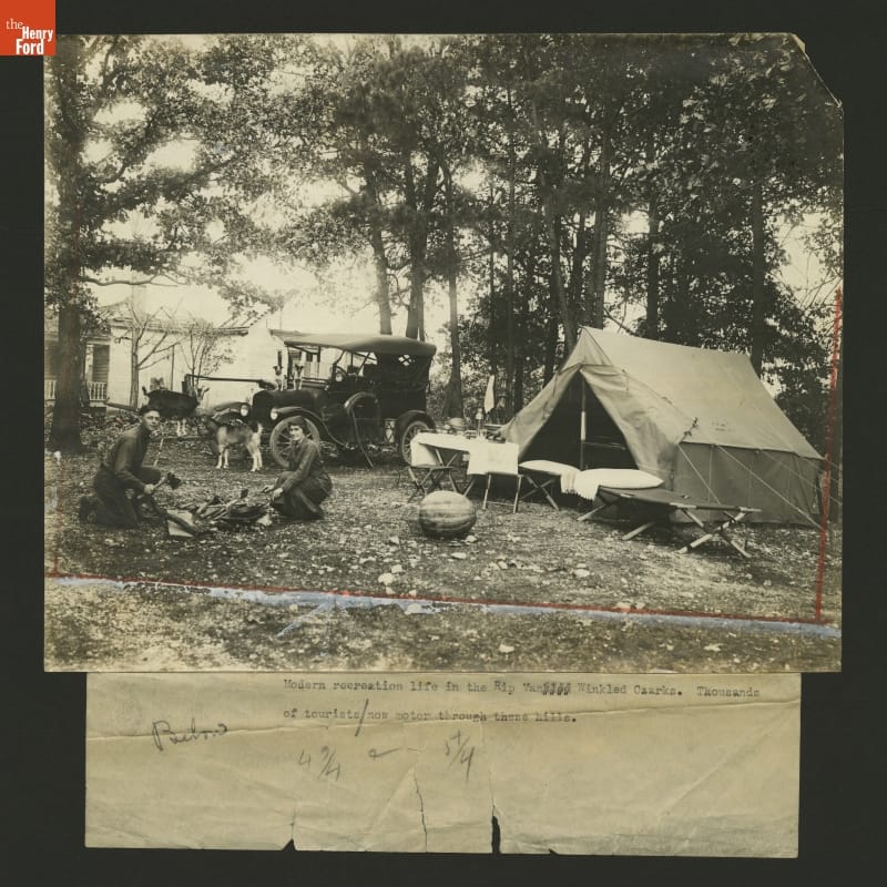 Cooking Over a Campfire in the Missouri Ozarks, 1923 Black-and-white photo of campsite with tent, people by a cooking fire, a Model T, two goats, and two dogs