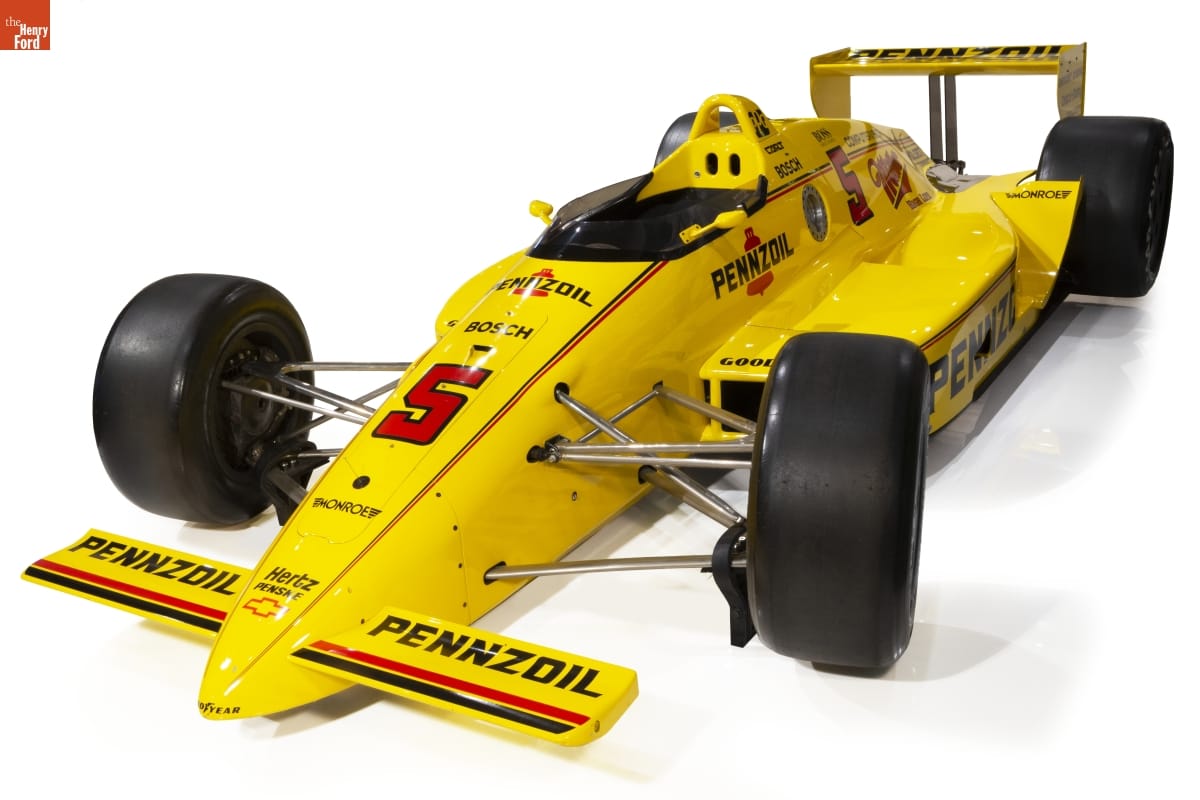 1988 Rick Mears Winning Indy Car Replica. On Loan from General Motors Heritage Center. Low, bright yellow race car with large wideset tires and black and red text and decoration