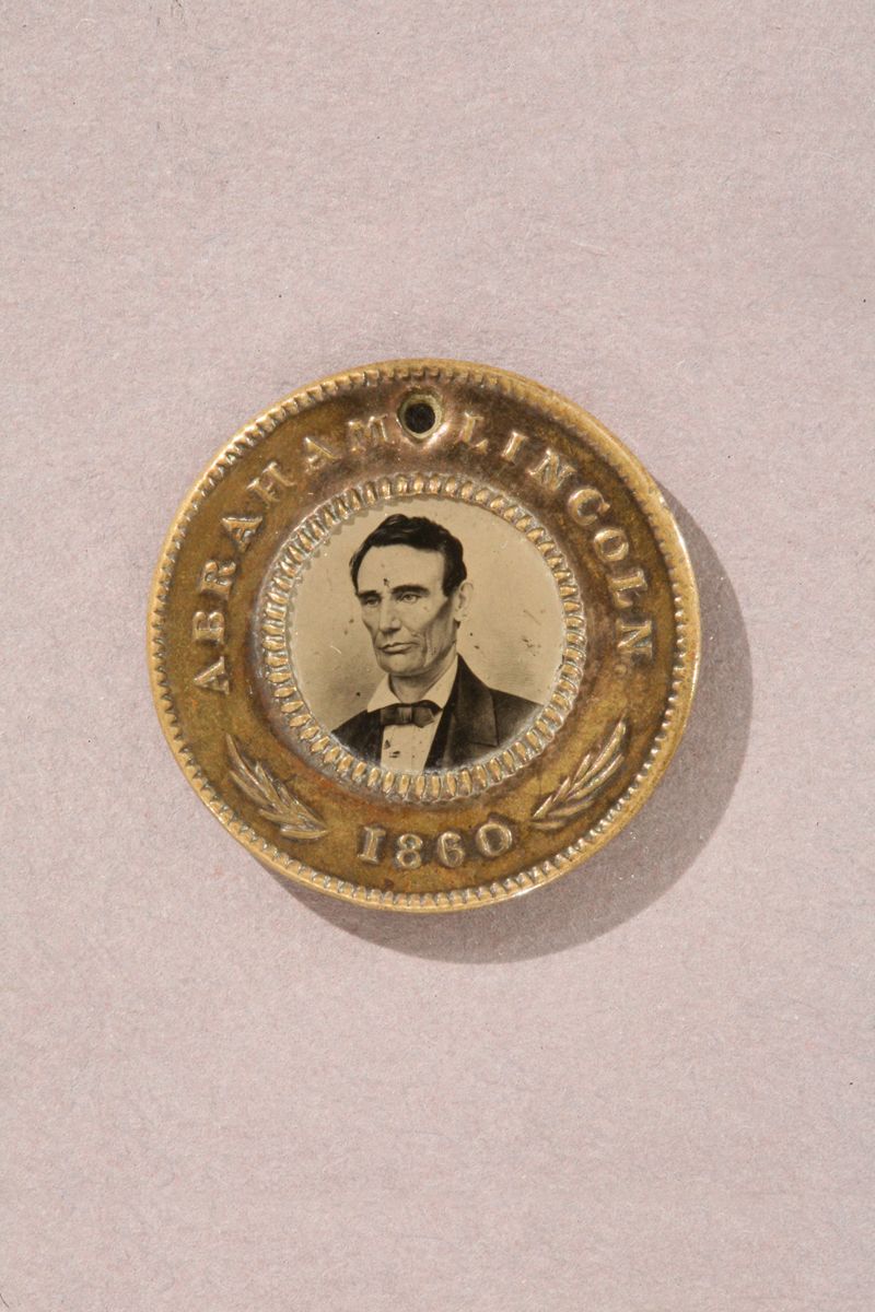 Abraham Lincoln and Hannibal Hamlin Campaign Button, 1860 Gold colored button with text "Abraham Lincoln 1860" and portrait of man in center