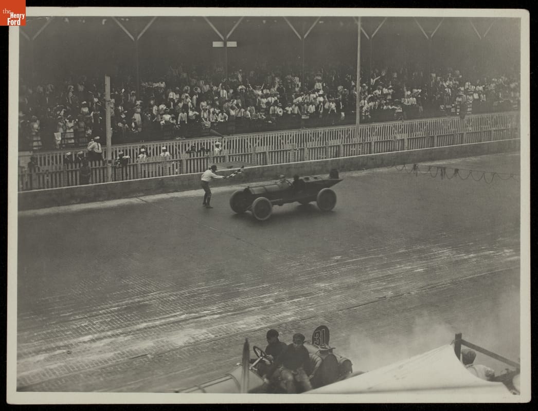 The Marmon Wasp Driven by Ray Harroun, Winner of the 1911 Indianapolis 500 Black-and-white photo of an old-fashioned race car on a dirt track in front of stands filled with fans