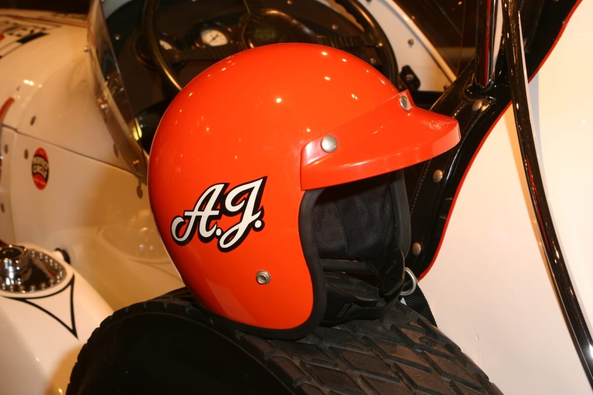 Racing Helmet Worn by A. J. Foyt, 1967-1969 Orange helmet with white initials "A.J." on side, sitting on wheel of white race car