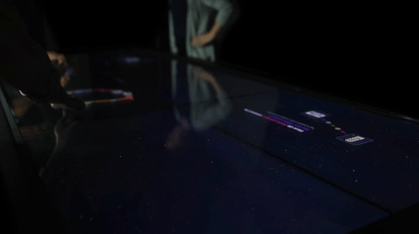 Our partners at Bluecadet trying out the table Video of people running their fingers over a large touch table, bringing up colorful strings and small images with text