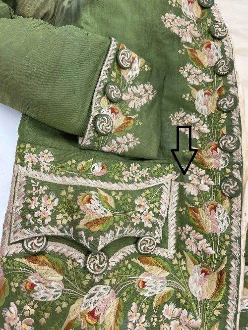 Showing cut to shorten jacket at the top right of the pocket Detail of moss-green suit pocket and part of cuff with elaborate embroidery; an arrow points to a seam coming off the top of the pocket