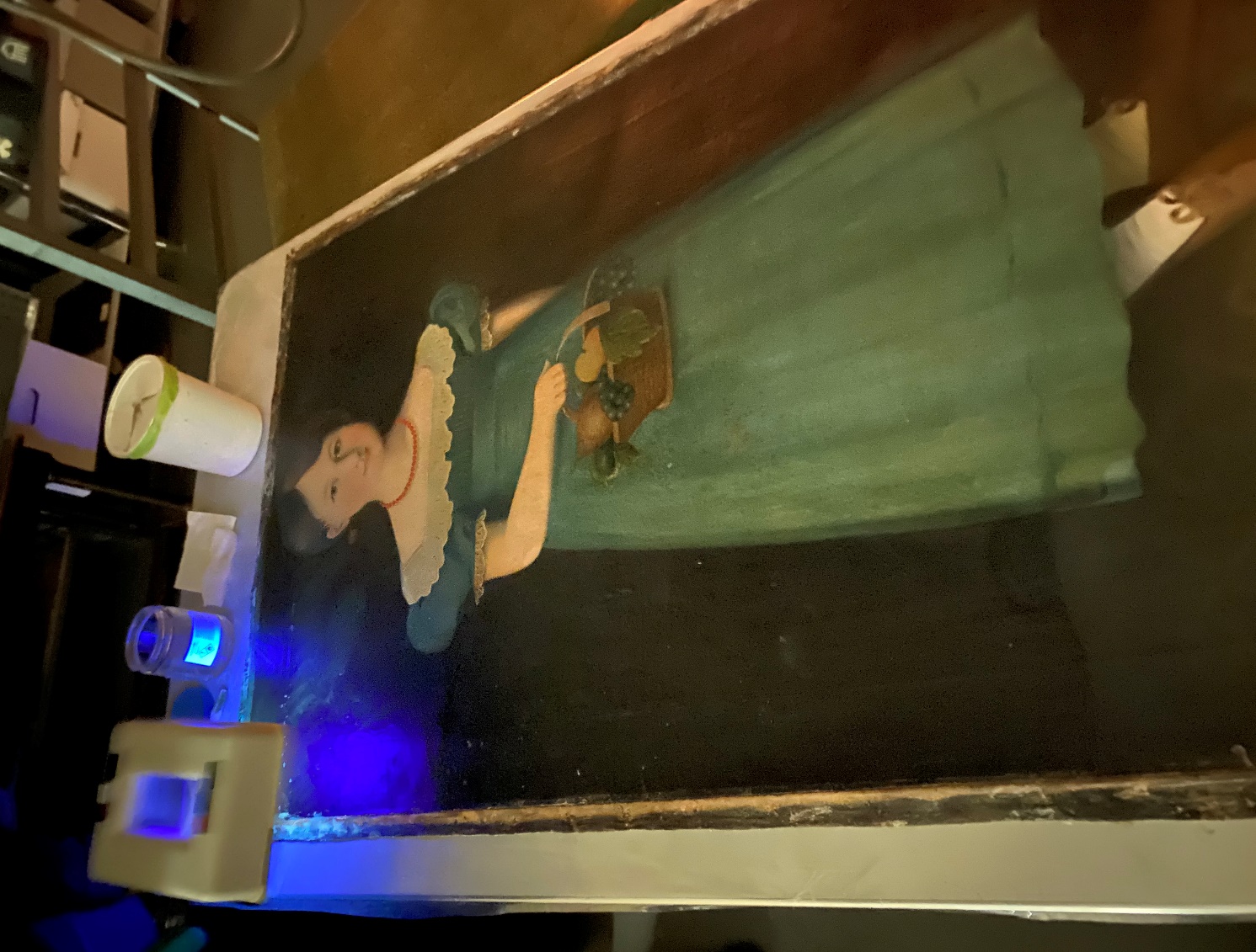 UV light to aid in cleaning Painting of girl in blue dress, laid flat on table with blue light and tools at one end