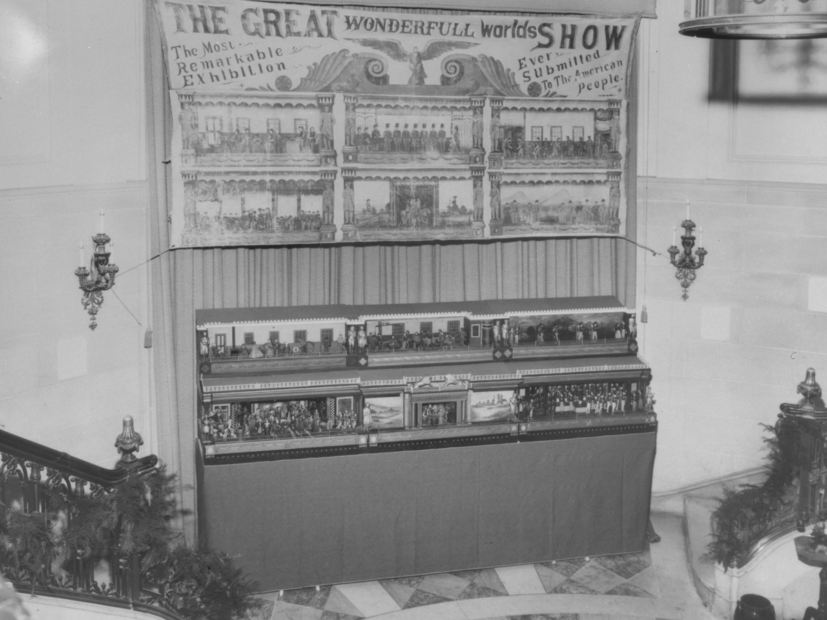 "The Busy World" Exhibit Exhibit with small wooden scenes on a platform underneath a banner