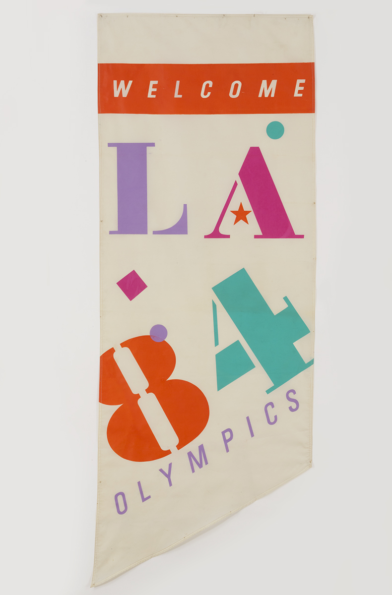 White banner with colorful graphic characters "L A 8 4" and additional text "WELCOME" and "OLYMPICS"
