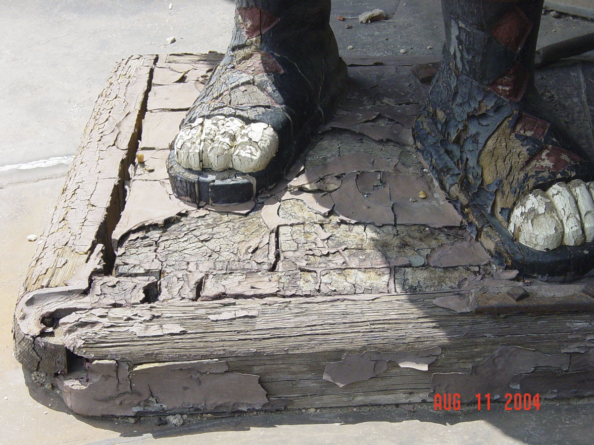 Deterioration on the feet of one of the giants. Statue base and sculpted feet of very cracked wood