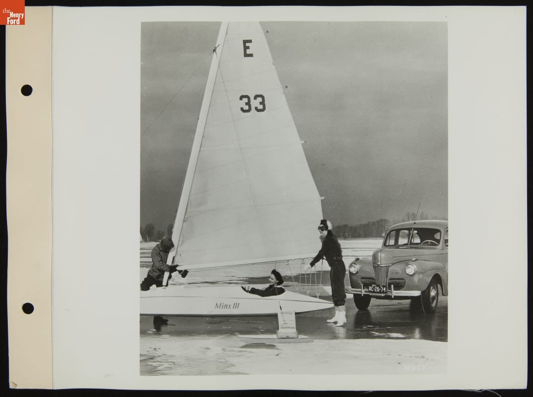 Women with Ice Boat and Ford Super Deluxe Fordor, February 1941 Woman sits in a long, low conveyance with sail and “Minx III” printed on side, on a bed of ice and snow, while two more women adjust the sail and a car is parked nearby