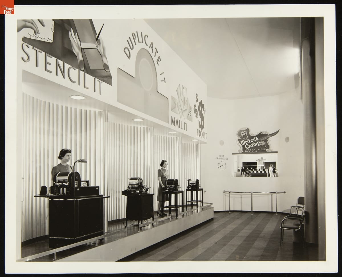 A.B. Dick Company Mimeograph Exhibit and "Writer's Cramp" Marionette Show at the New York World's Fair, 1939 Room with display of office equipment and two women standing by it to the left, and puppet show in back