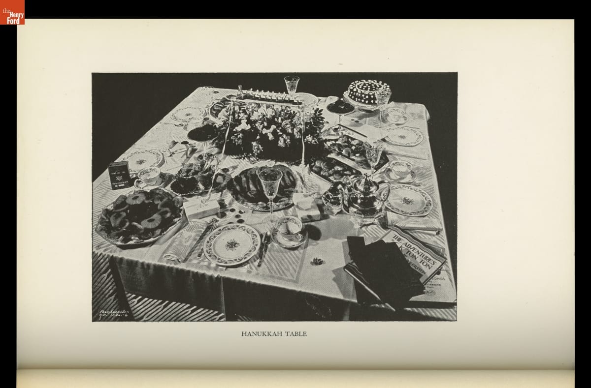 Book, "Jewish Home Beautiful," 1955 / page 25 Image labeled "Hanukkah Table" of decorated table with place settings, food, books