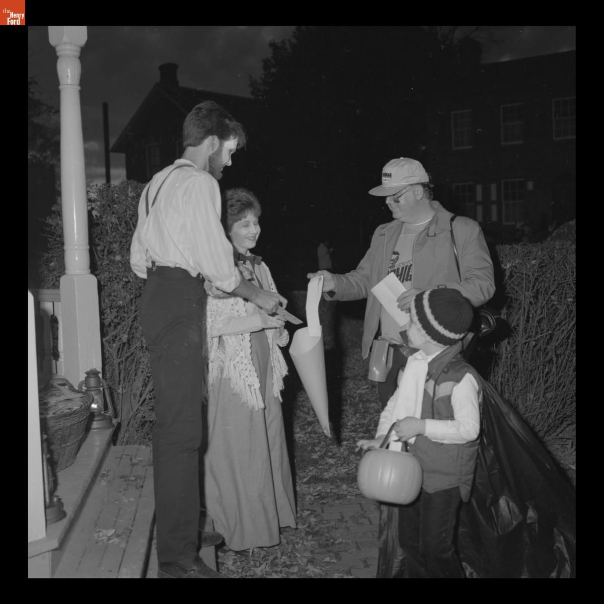 Man and woman wearing historical clothing and facepaint hand candy to man and little boy