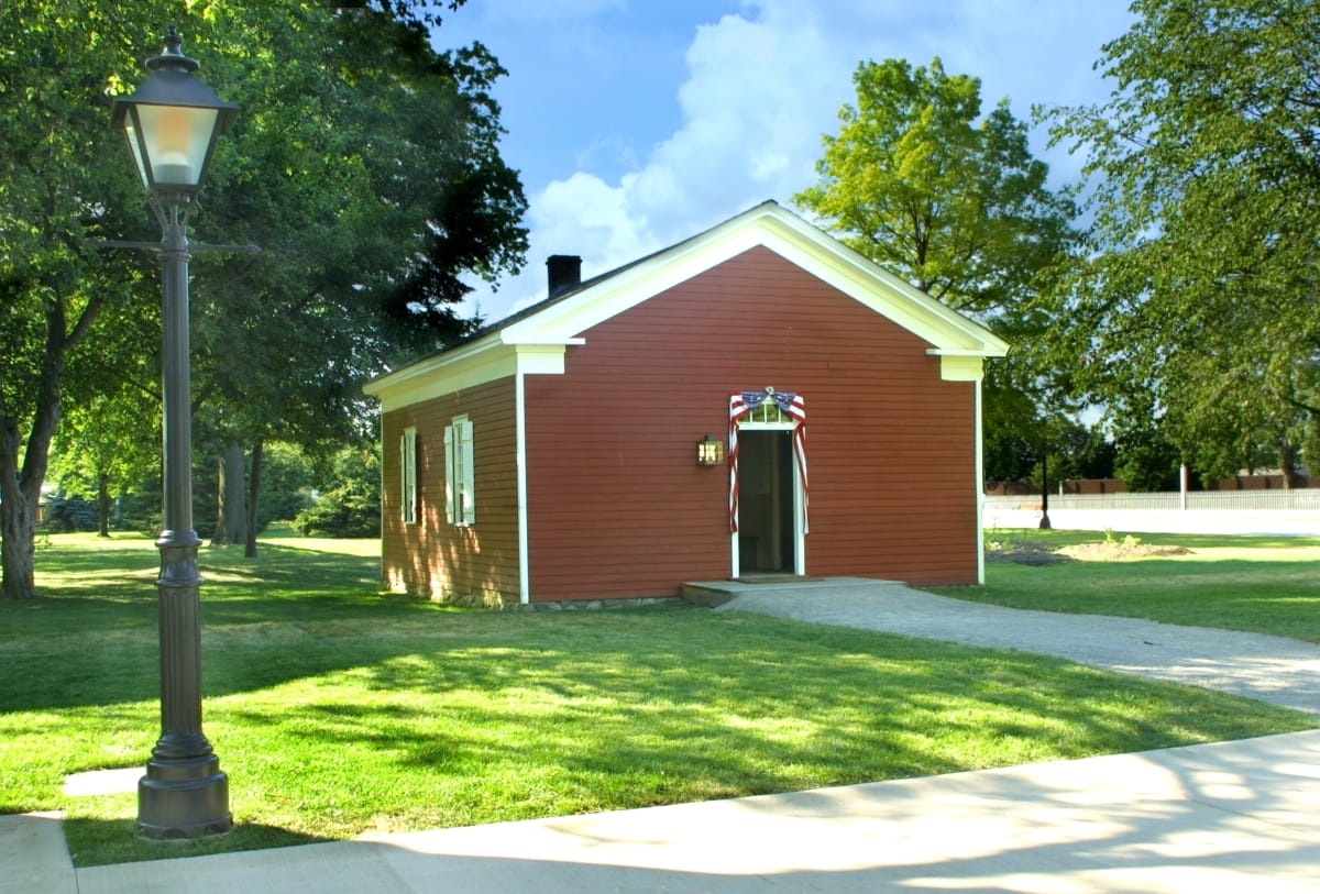 Dr. Howard's Office Small red building with white trim set on green lawn with trees, roads, and a streetlamp nearby