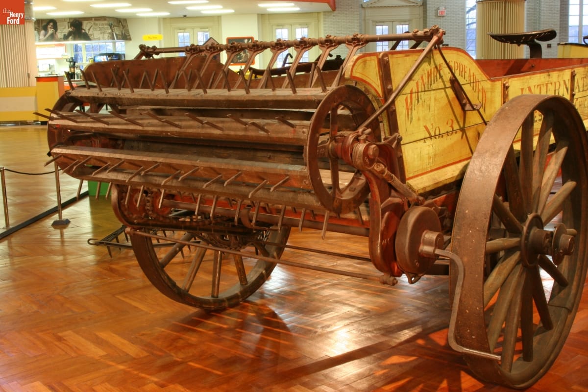 International Harvester Manure Spreader, circa 1905 Wooden beater with spikes on the end of a yellow wooden wagon in a large room