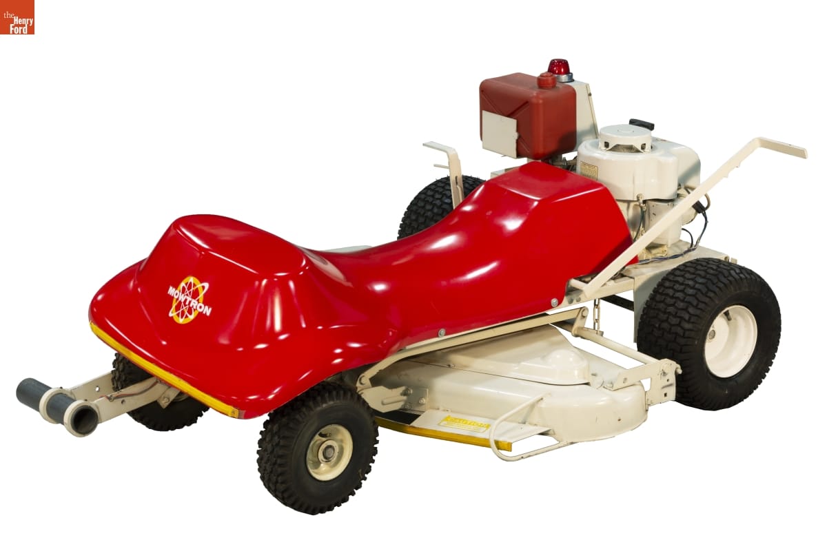 Mowtron Mower, Used as a Display Model, 1974 Low lawnmower with red plastic body on white platform with four black wheel