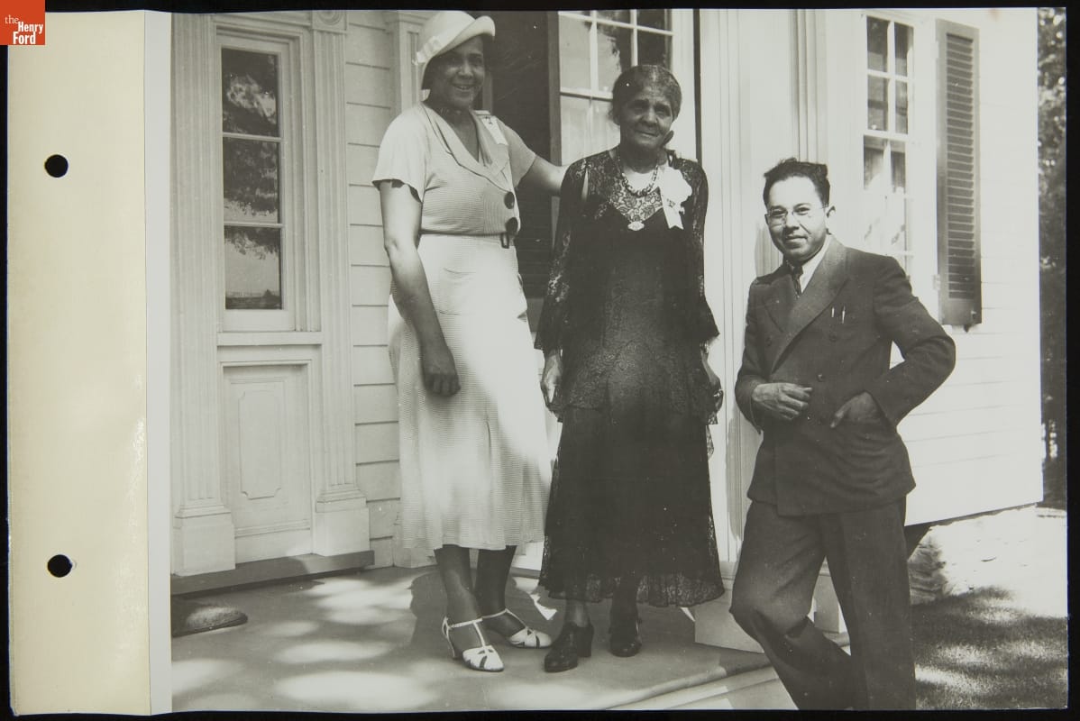 Two women and one man pose for a photo on the porch or front steps of a house