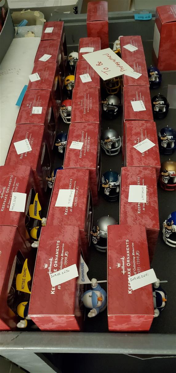 Ornaments lined up on a cart, ready to be photographed. Red boxes lined up, with an ornament (mostly mini football helmets) in front of each