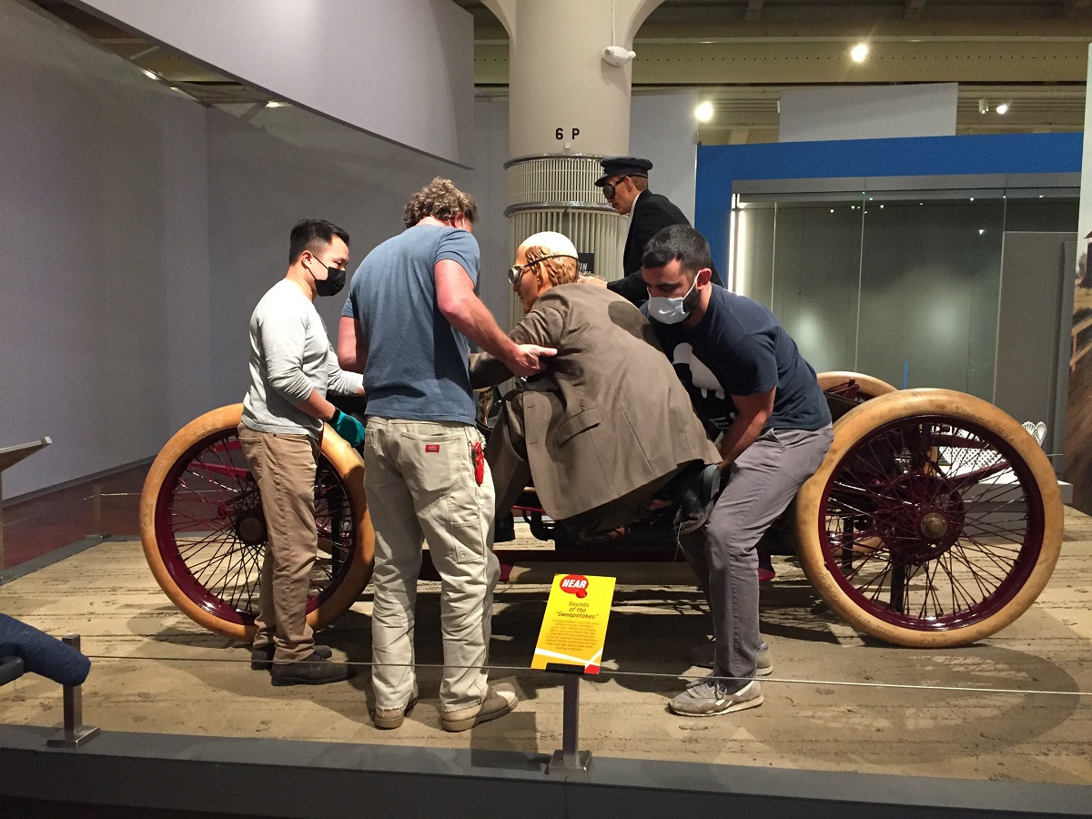 Placing Spider Huff on the Sweepstakes Three men move a mannequin into place on the running board of a car; another mannequin is inside the car