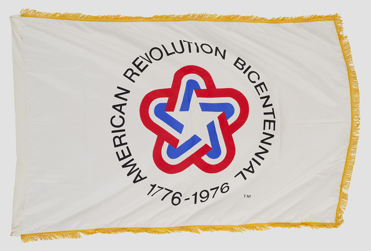 United States Bicentennial Flag, circa 1976 Gold-fringed white flag with rounded star in red, white, and blue and text "American Revolution Bicentennial 1776-1976"