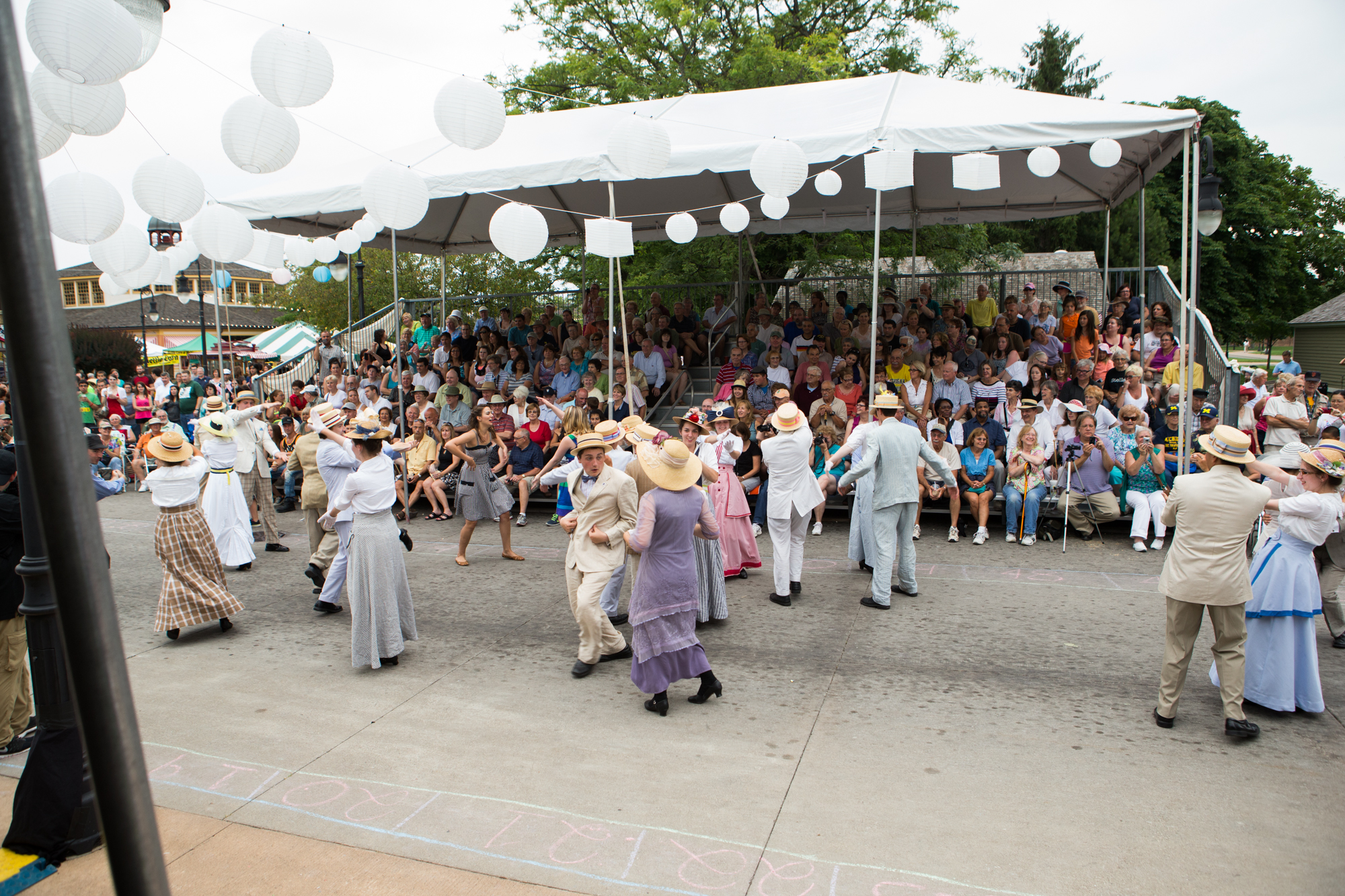 Dancers in vintage costumes on concrete road with crowd watching
