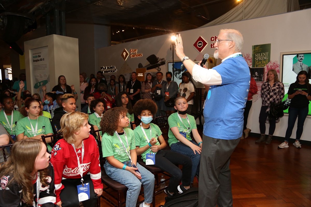 Invention Convention Michigan emcee Mike Moseley A man in a blue t-shirt talks to a group of children and adults
