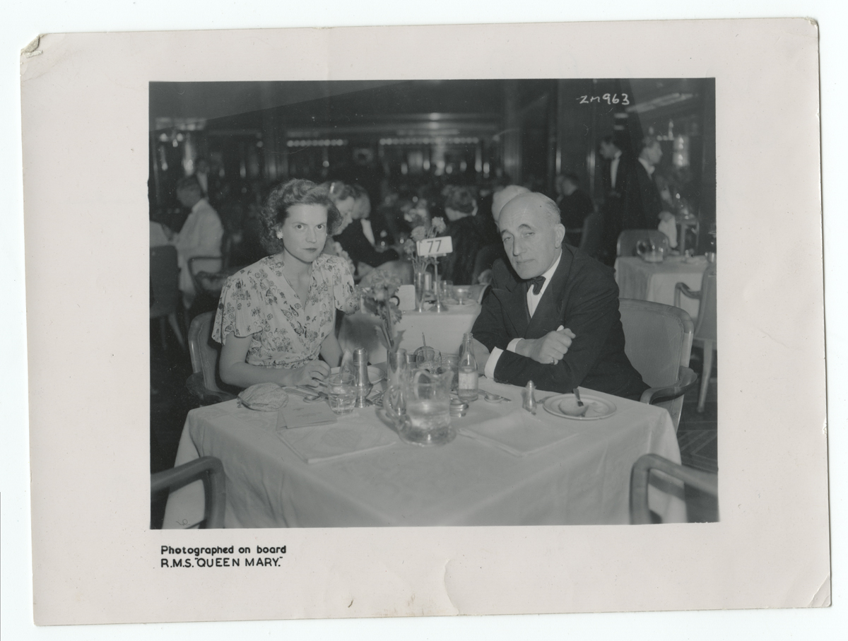 Augusta Roddis at lunch in the first-class dining room of the RMS Queen Mary, September 1949 Black-and-white photo of a woman and man seated at a tablecloth-covered table among other diners