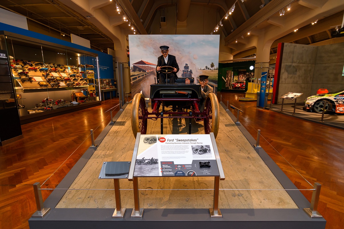 Henry Ford and Spider Huff on the Sweepstakes in Driven to Win in Henry Ford Museum of American Innovation Museum display with open car with mannequin behind wheel; other displays visible nearby