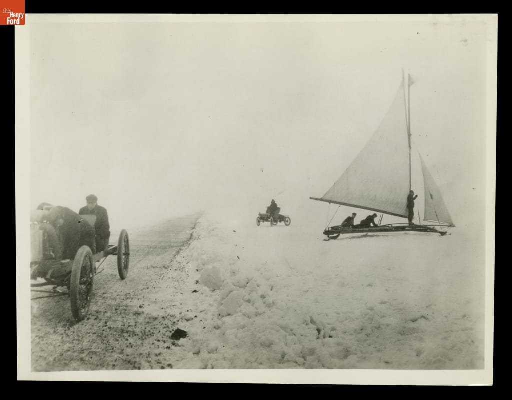 Henry Ford and Spider Huff Driving Arrow Racer on Lake Saint Clair, 1904 Car with two people in it on road or path on left side; on right side a conveyance with a sail and another car, each with people in them, sit in snow