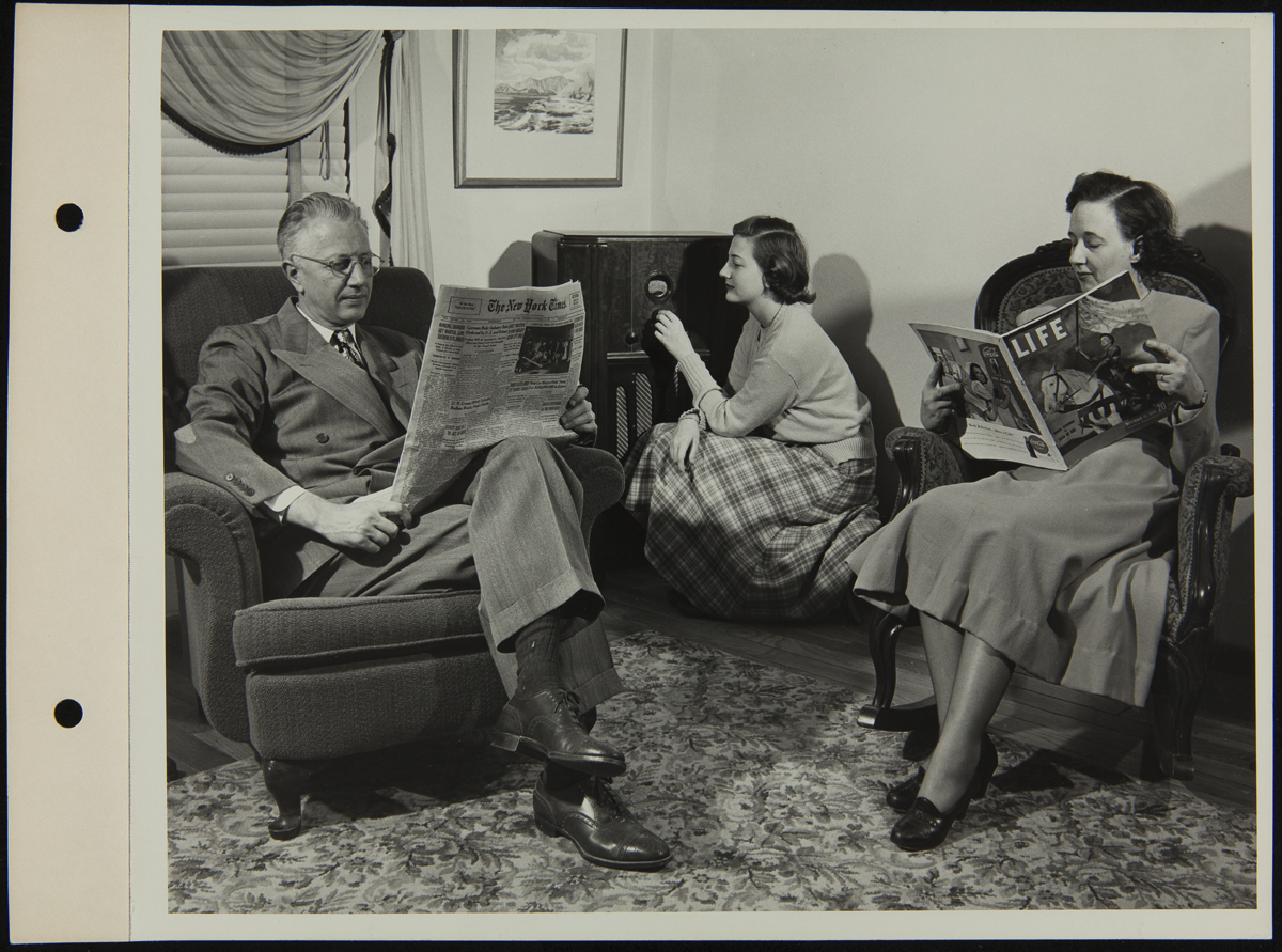 Man and woman sitting in chairs, reading, while teen girl kneels by a radio