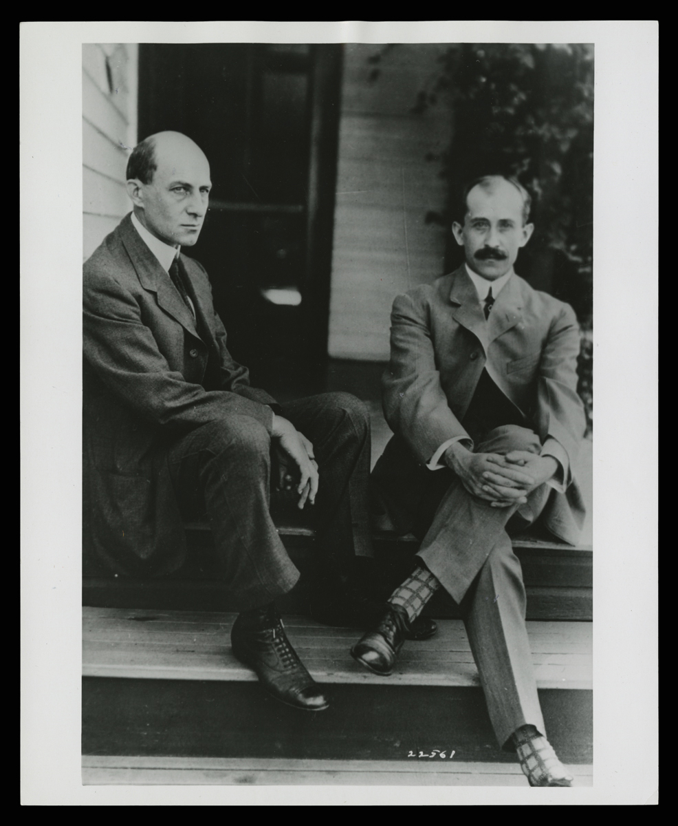 Two men in suits sit on porch steps