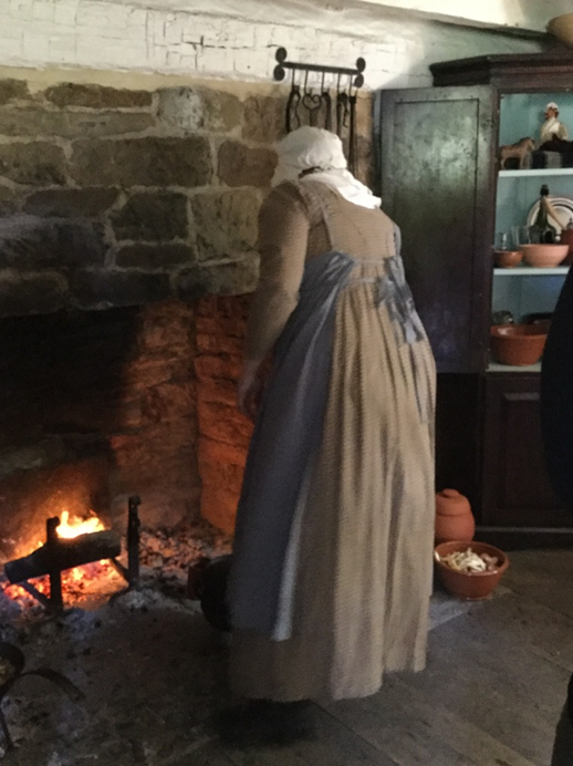 Presenter cooking over the fireplace in the William Holmes McGuffey Birthplace, 2018 Woman in long simple dress and apron bends over a fire in a large stone fireplace