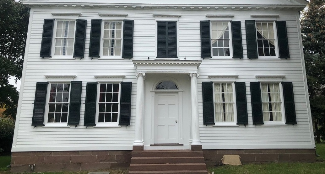 The front façade of the Noah Webster Home, showing the balance of windows and the door Front façade of a white house with symmetrical windows with black shutters, and closed black shutters above the front door