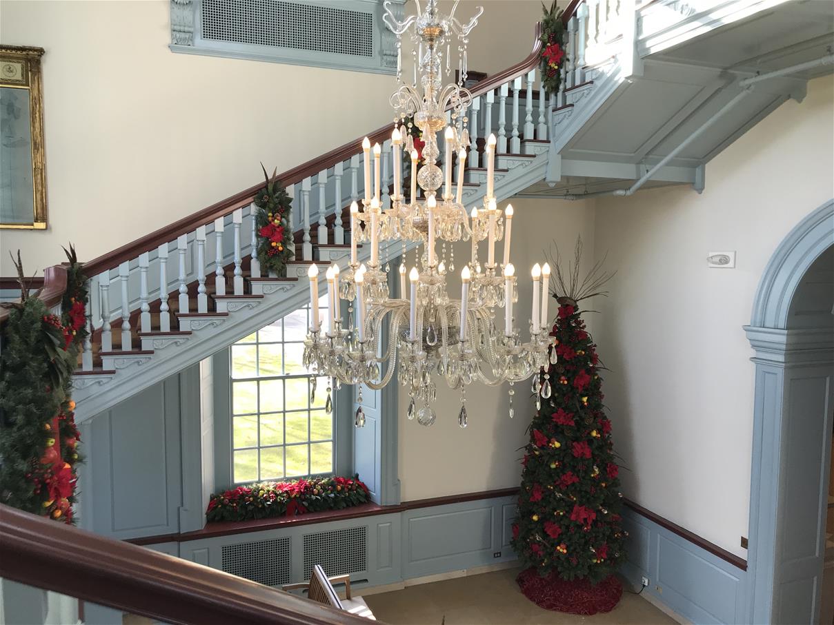 The Clocktower in Henry Ford Museum of American Innovation decorated for the holidays White-and-light-blue room with staircase and elaborate chandelier, decorated with Christmas trees and greenery
