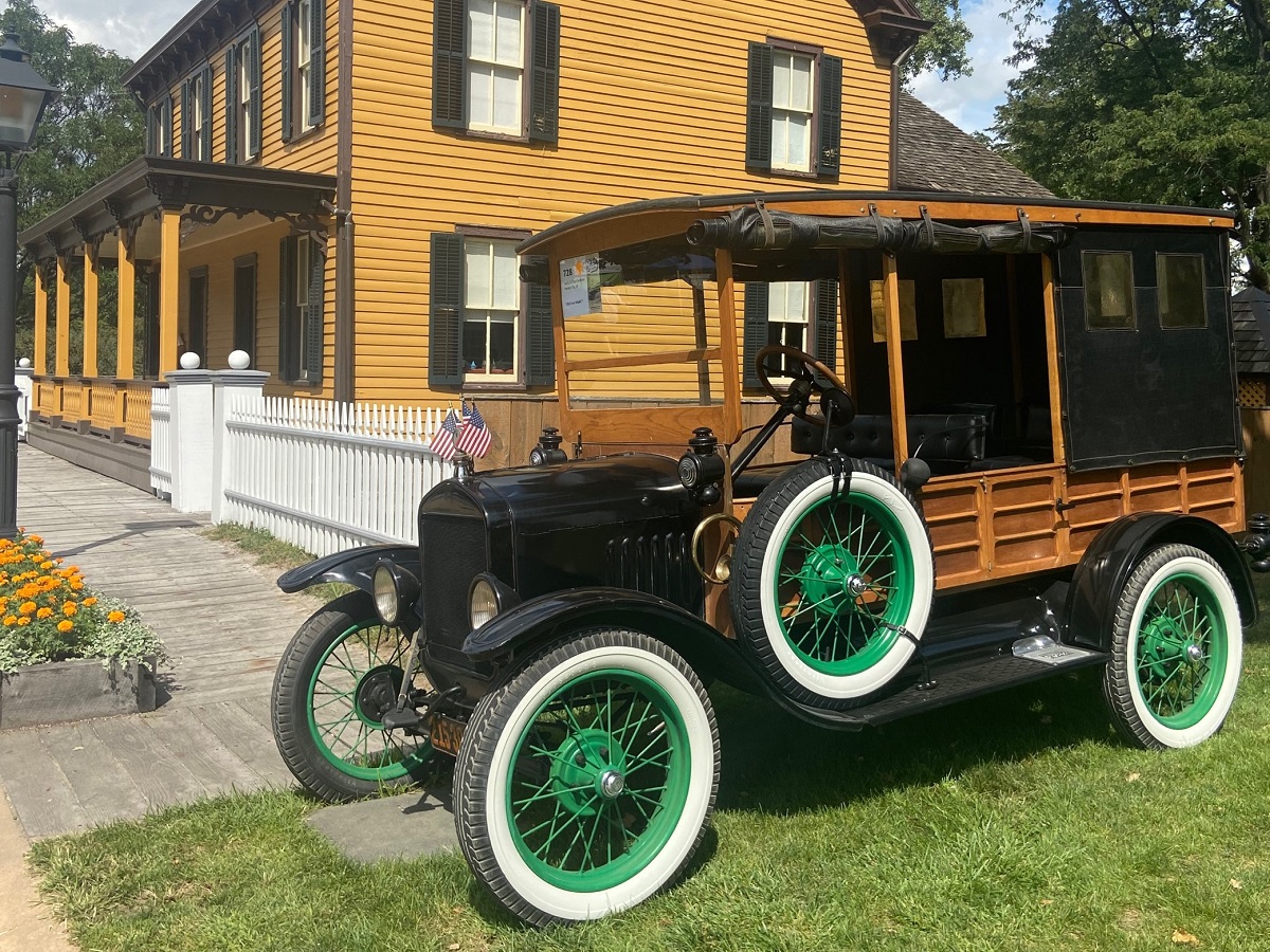1924 Ford Model T depot hack at Old Car Festival 2022 Old-fashioned truck with wooden sides and whitewall tires with green rims, parked in front of a mustard-colored wooden building