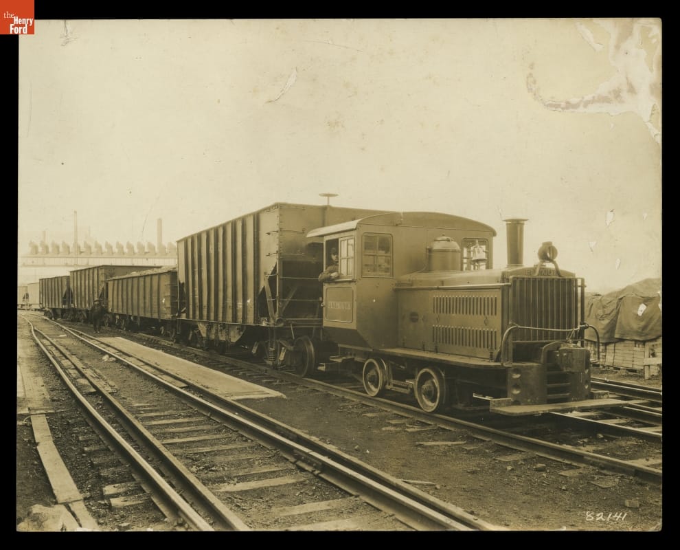 Engineer Charles Vaughn in Plymouth Locomotive at Mistersky Power Plant, West Jefferson Avenue, Detroit, Michigan, circa 1930 Black-and-white photo of small locomotive pulling rail cars on railroad tracks