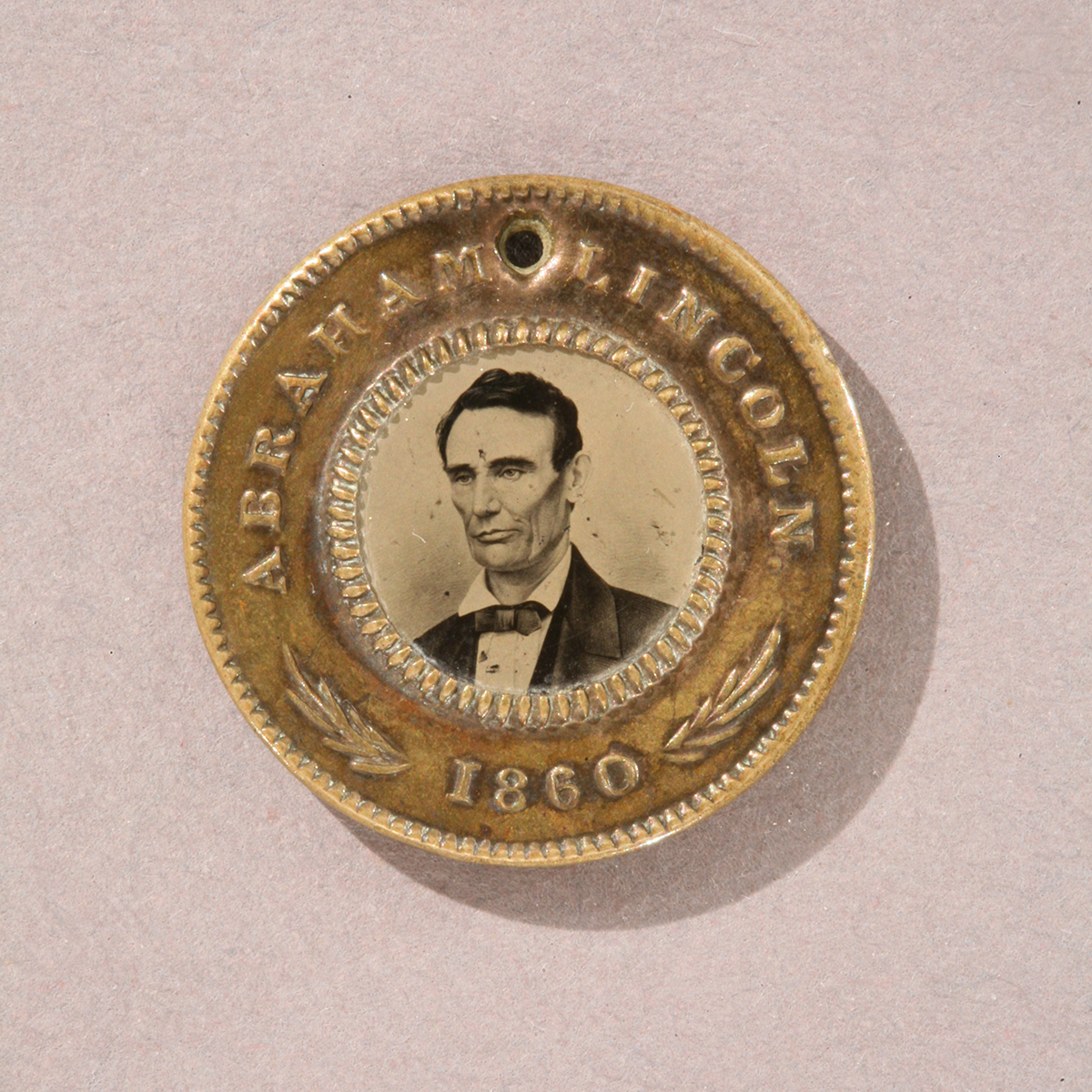 Round gold token with image of man’s shoulders and head in the middle and text “Abraham Lincoln 1860” around edge