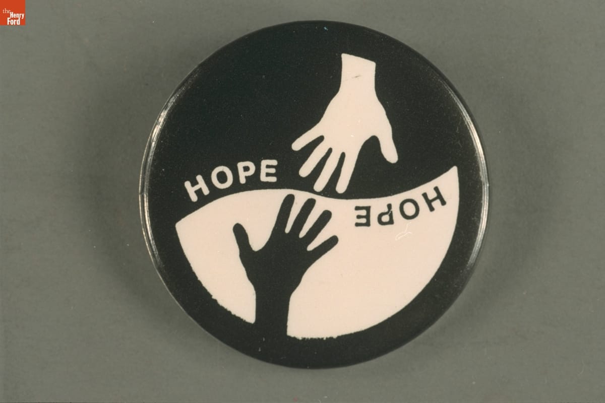 Round button with top portion displaying a white hand and word "hope" on a black background, and the bottom half with the same elements but black and white reversed
