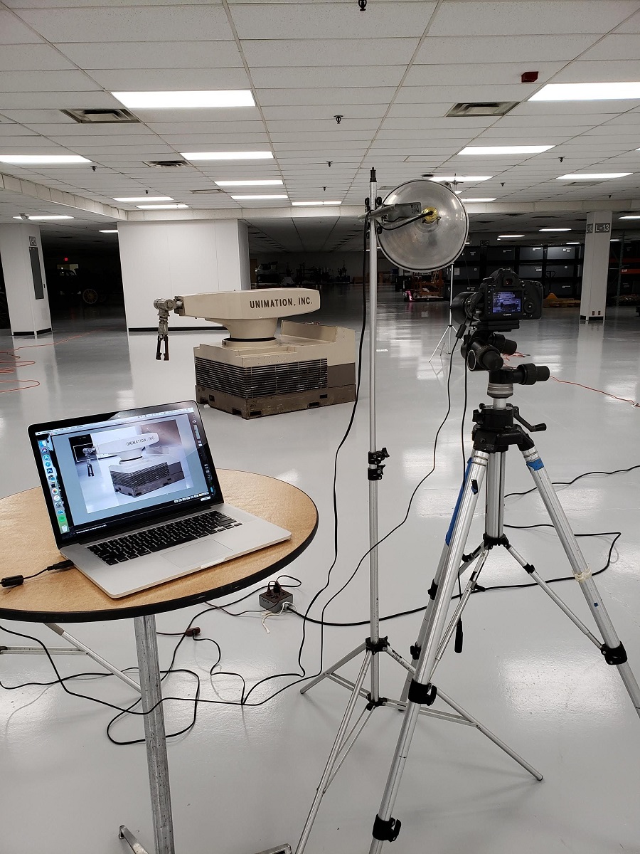Photographing the Unimate Large, squat robot with swing arm in the middle of a large space; photo on tripod and tethered laptop computer on table in the foreground