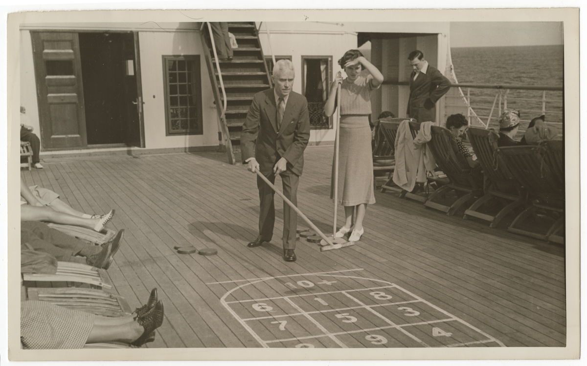 Hamilton Roddis and his daughter Augusta play shuffleboard Black and white photo of man in suit and woman in dress playing shuffleboard on a boat with passengers in lounge chairs nearby