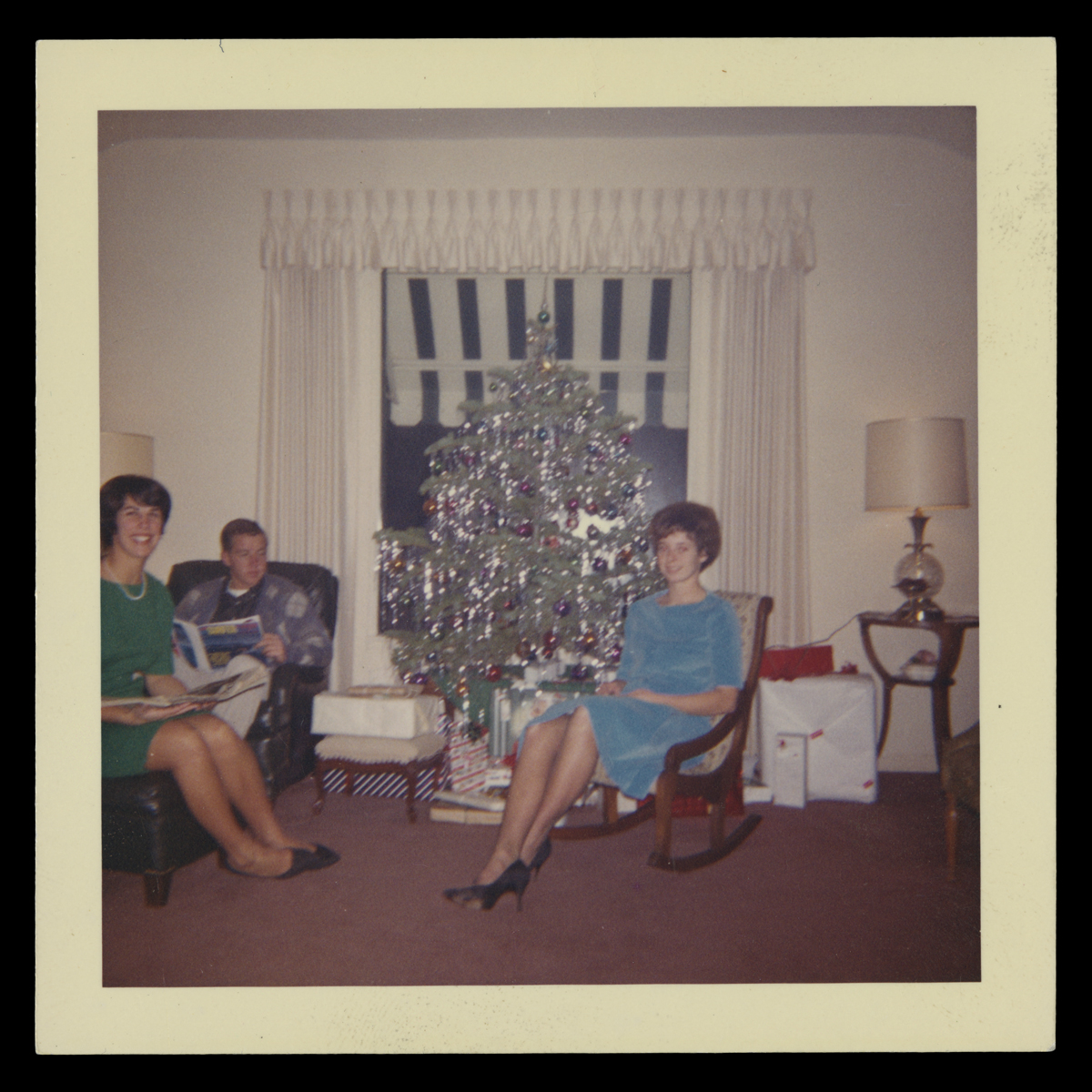 Two women and one man seated in a room around a silver aluminum Christmas tree