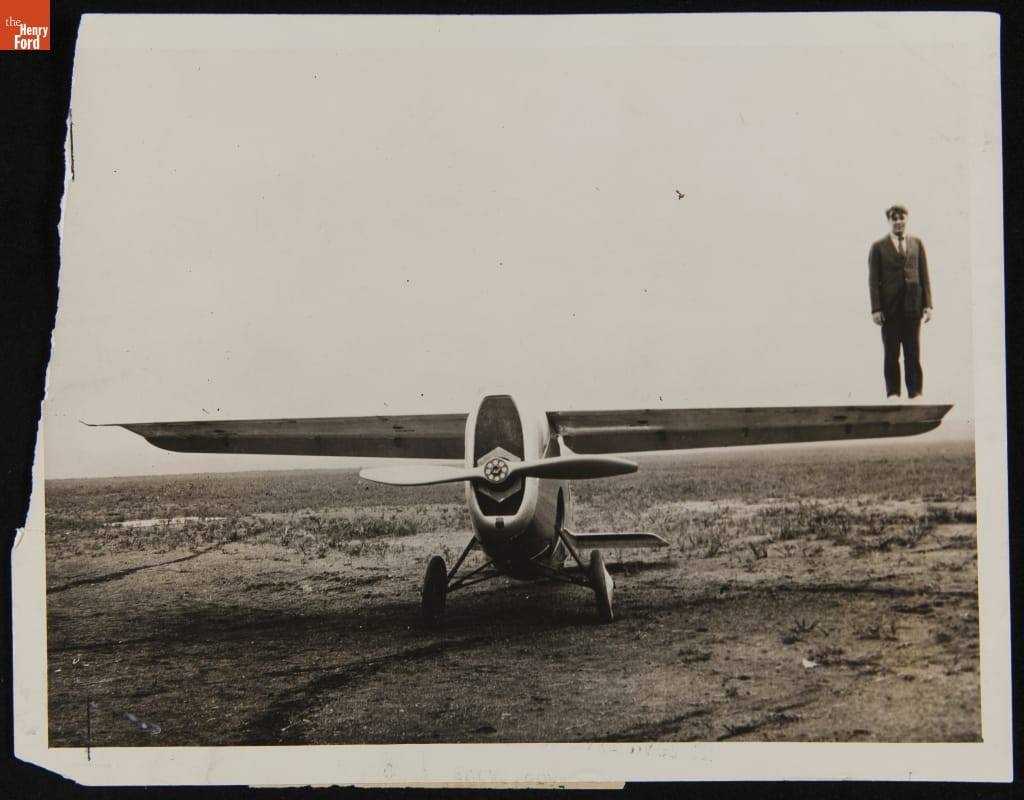 Pilot Howard Rinehart Standing on Wing of the Dayton Wright RB-1 Racer, August 1920 Black-and-white photo of man standing on top of end of wing of small airplane parked in large open field