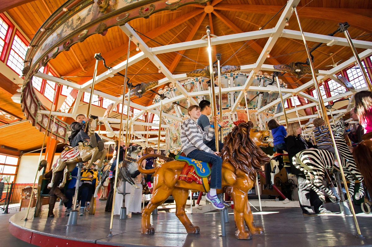 Herschell-Spillman Carousel Low-angle photo of a carousel in a wooden structure with children riding carved animals