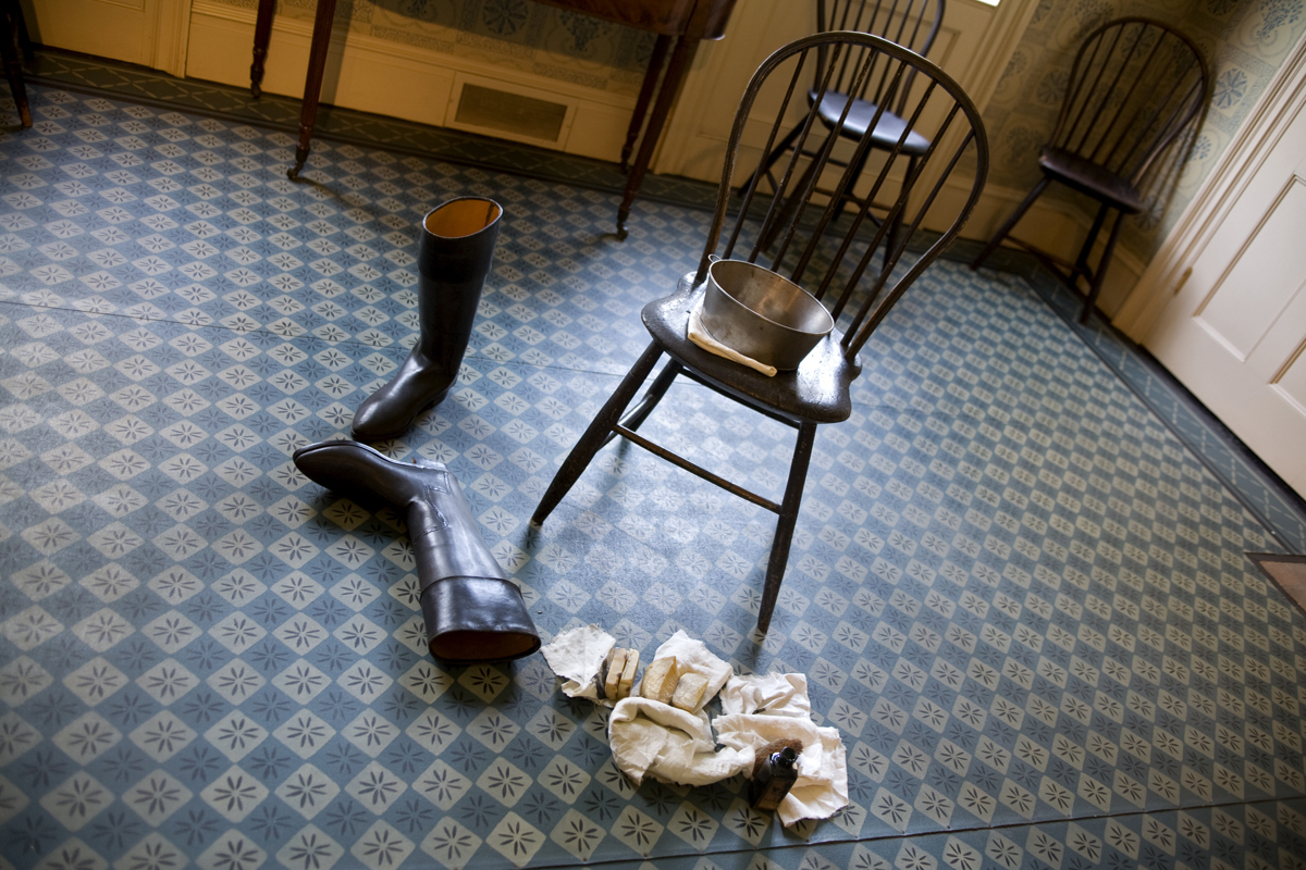 Pair of boots lying on patterned blue floor next to chair with tub; rags nearby