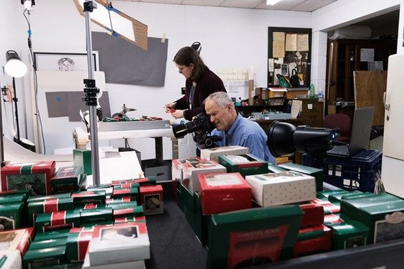 Photographing the ornaments. GIF cycling through two images of a man and woman with boxes of ornaments and camera