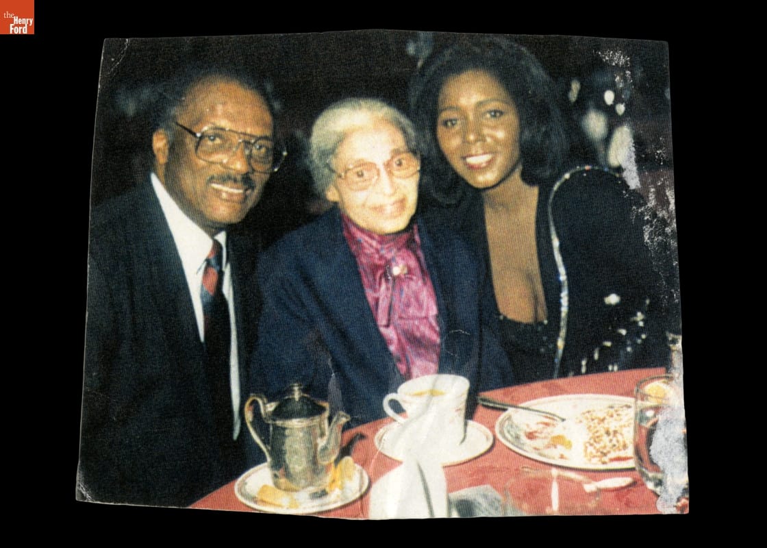Three formally-dressed people smile and pose for the camera at a dining table